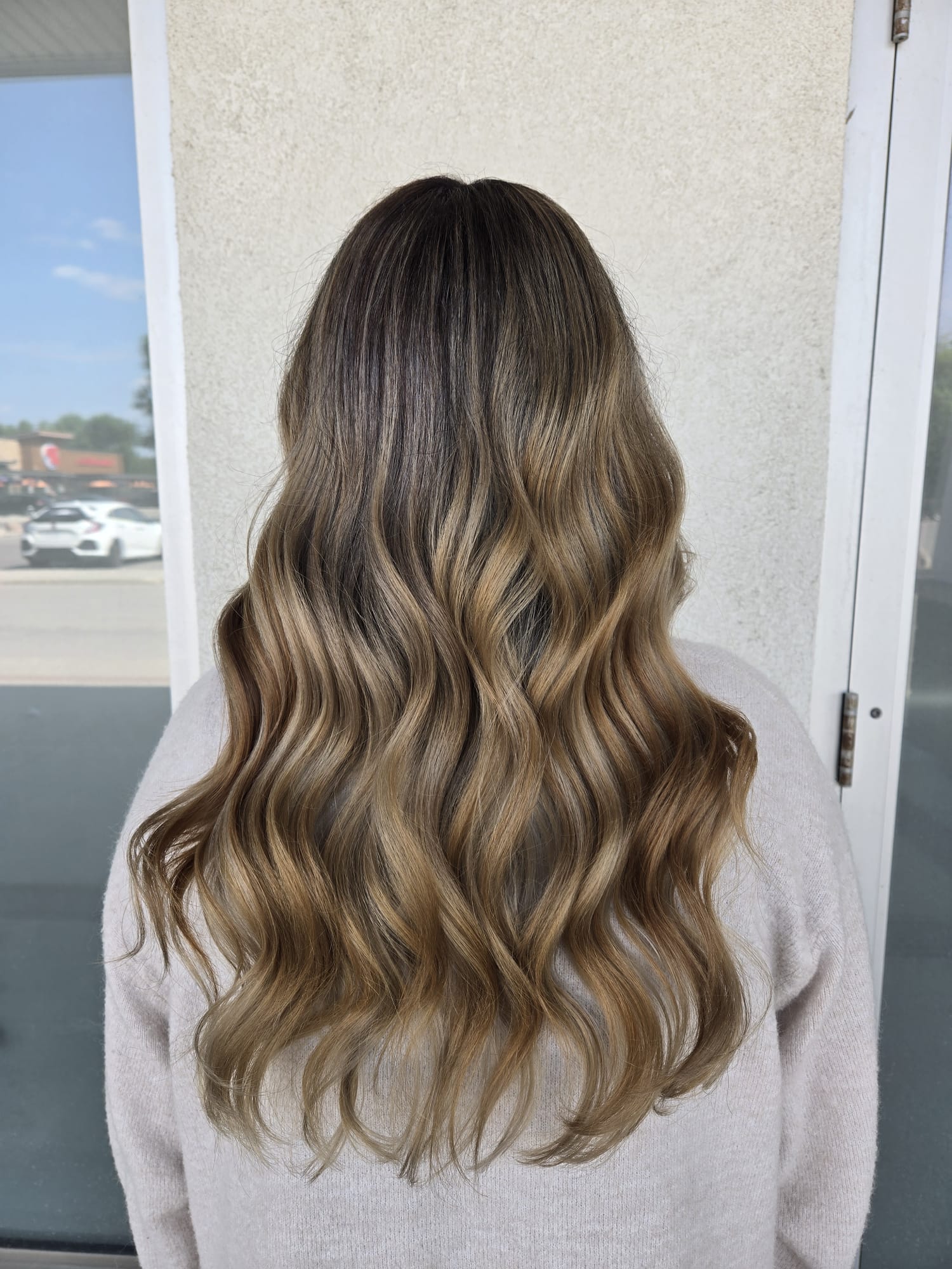 A girl with curly brown hair poses after getting a balayage in Winnipeg.
