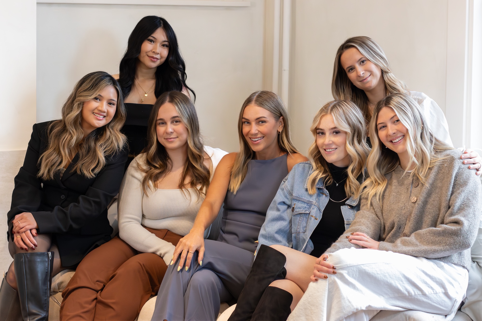 A group of young, female Grace Hill Salon and Spa stylists sit together on a couch.